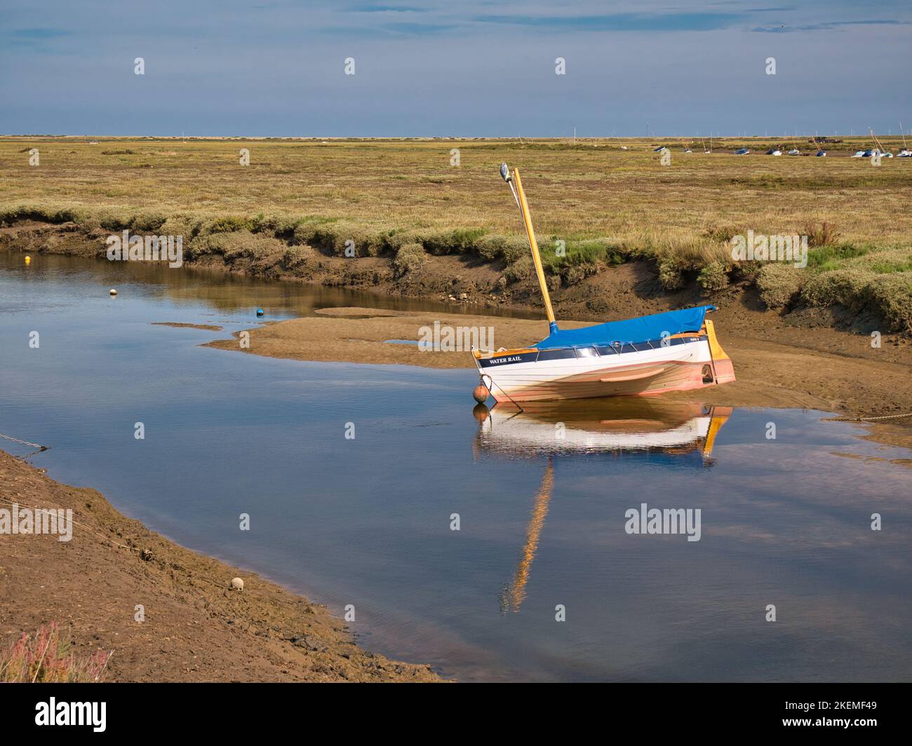 Una barca per il tempo libero ormeggiata in un canale verso il mare sulla costa nord del Norfolk. Preso in una giornata di sole con nuvola di luce e un cielo blu. Foto Stock