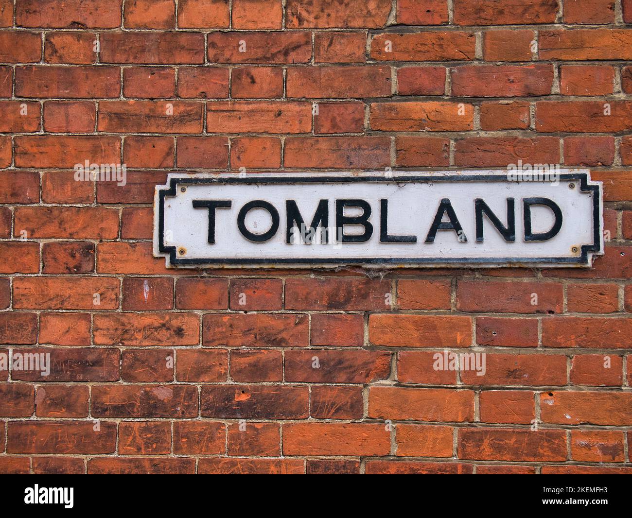 Un cartello in ghisa bianca con scritte nere su un vecchio muro di mattoni rossi mostra la posizione di Tombland a Norwich, Regno Unito. Foto Stock