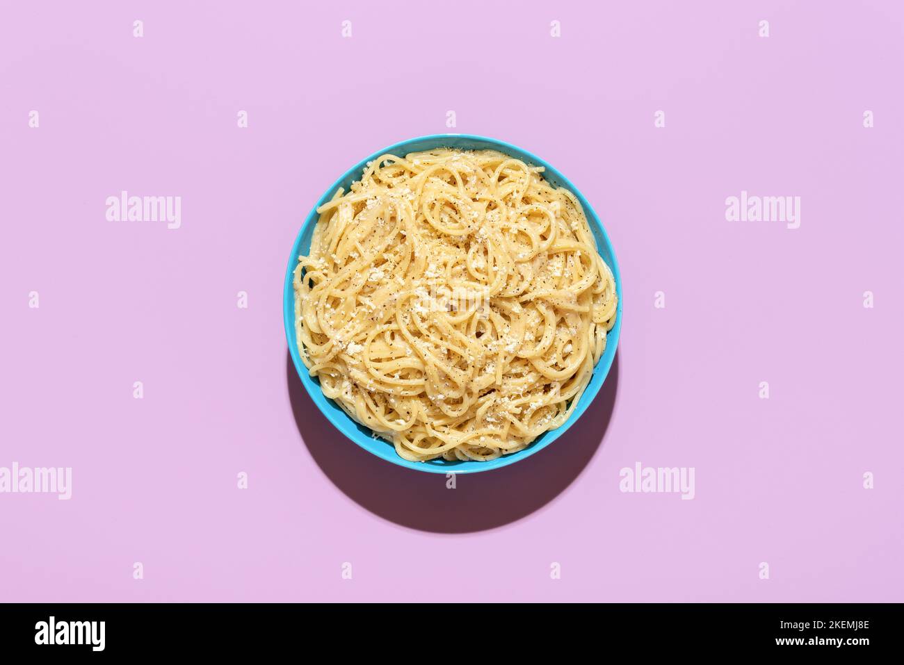 Vista sopra con una porzione di pasta cacio e pepe, minimalista su un tavolo viola. Delizioso piatto italiano, spaghetti con formaggio grattugiato e pepa nera Foto Stock