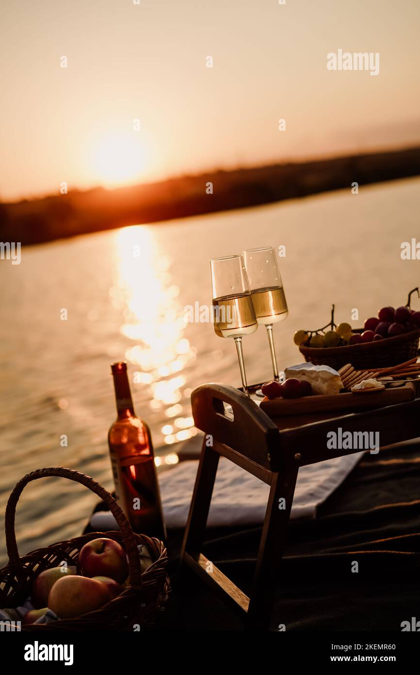 Incredibile tramonto sul lago, vino bianco, torta di frutta, mele, uva, formaggio brie, biscotti. Picnic estetico autunnale. Foto Stock