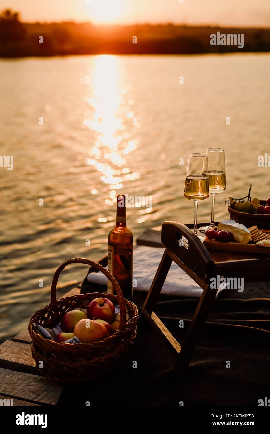Incredibile tramonto sul lago, vino bianco, torta di frutta, mele, uva, formaggio brie, biscotti. Picnic estetico autunnale. Foto Stock