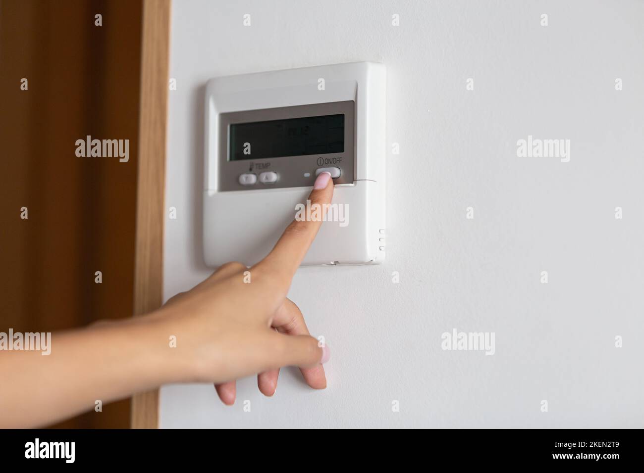 Primo piano della mano di una giovane donna premendo il pulsante on/off del condizionatore d'aria o del riscaldatore Foto Stock