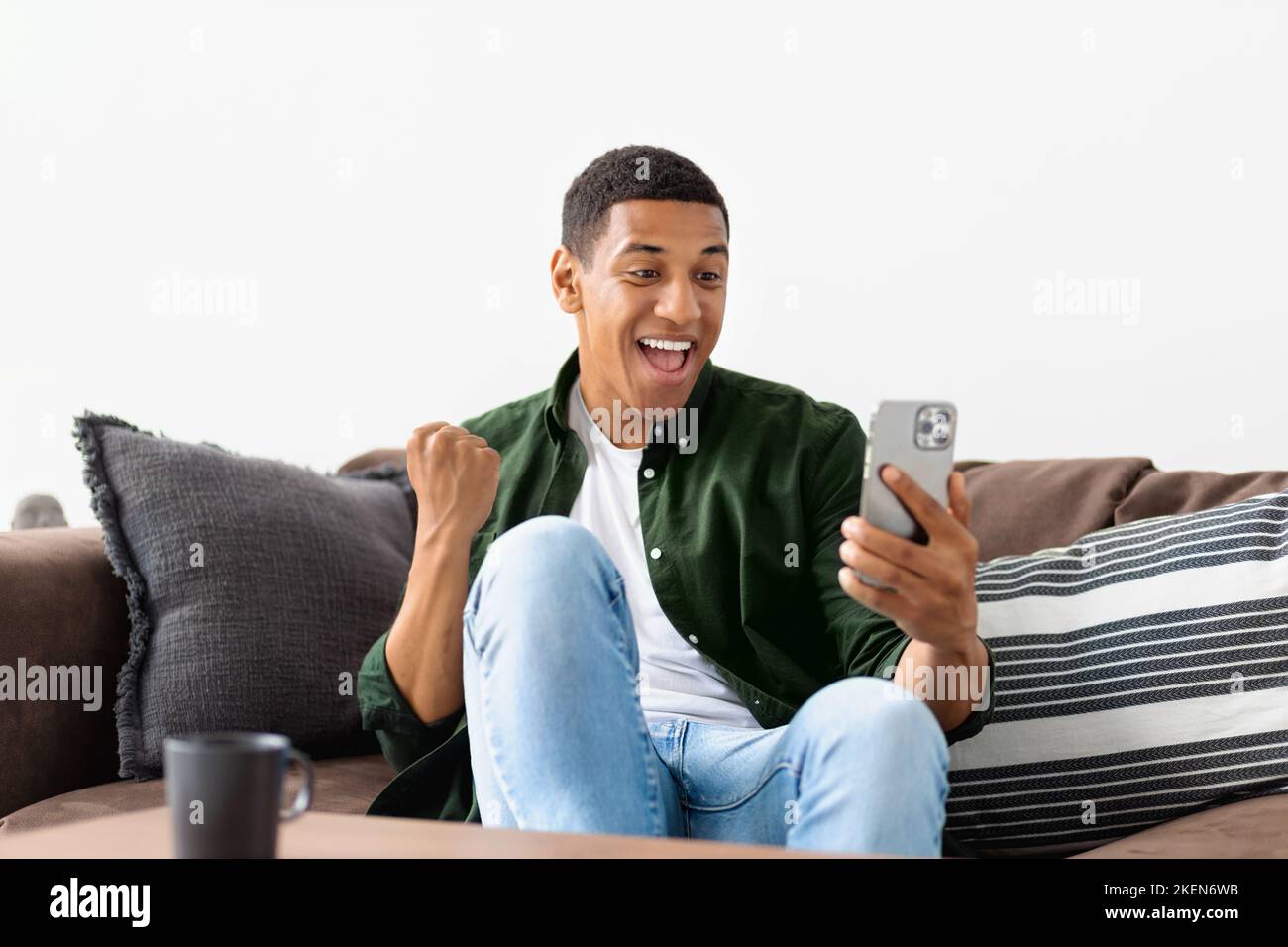 Giovane afro-americano guardando lo schermo del telefono cellulare e urlando, ottiene buone notizie, concetto di successo Foto Stock