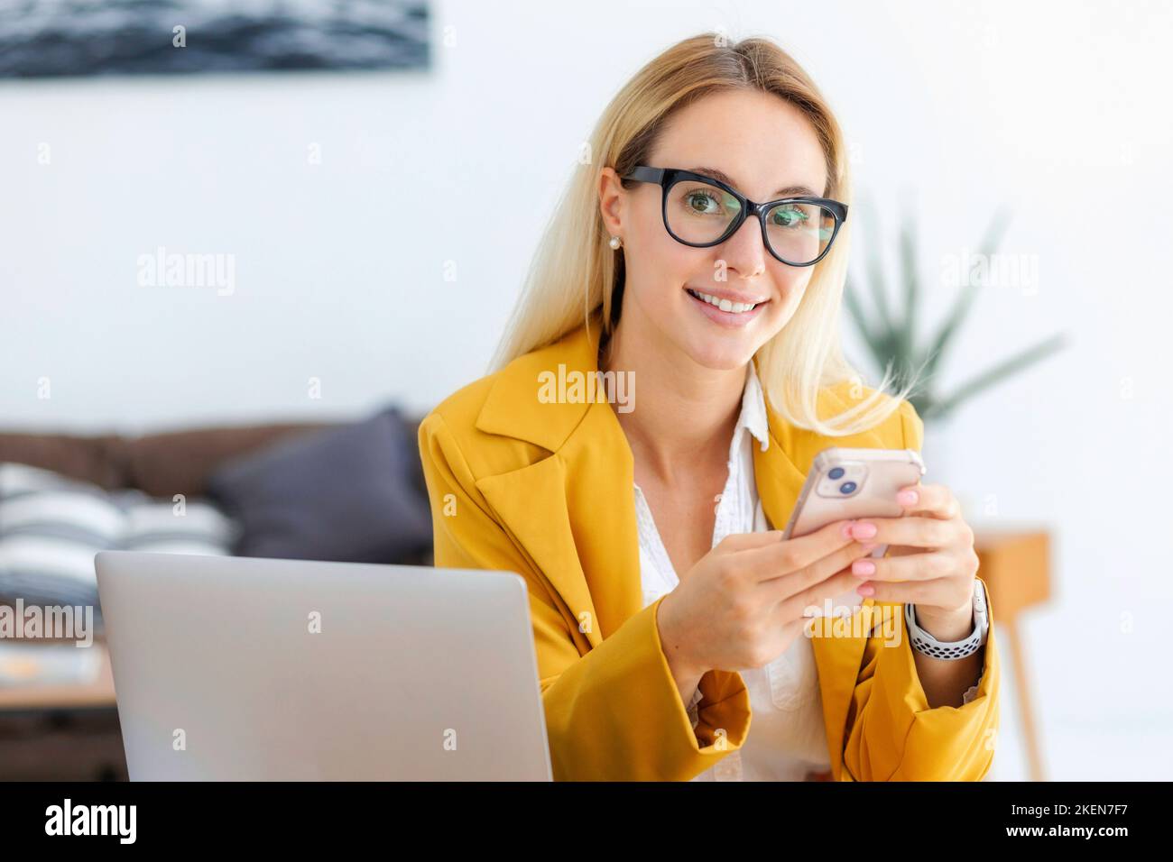 Felice sorridente fidata donna dirigente seduto sul posto di lavoro in un ufficio moderno, lavorare con il telefono cellulare Foto Stock