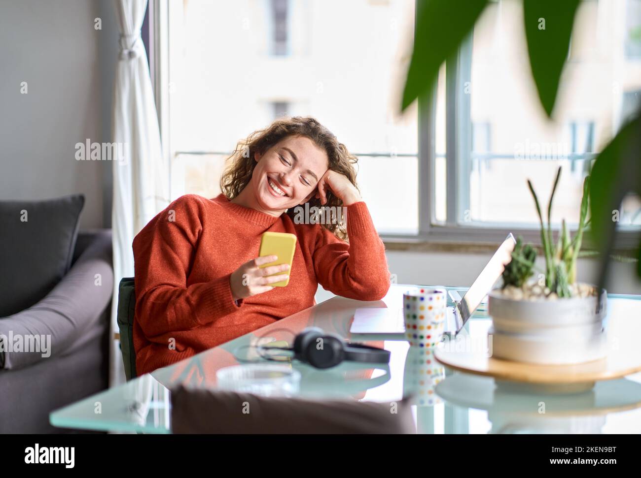 Giovane donna sorridente che tiene il telefono cellulare a casa con lo smartphone. Foto Stock