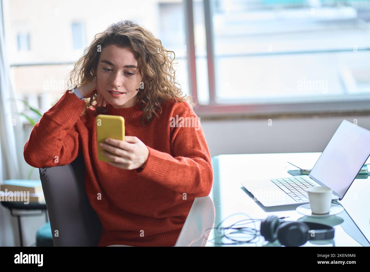 Giovane donna graziosa che usa il telefono cellulare mentre lavora a casa. Foto Stock