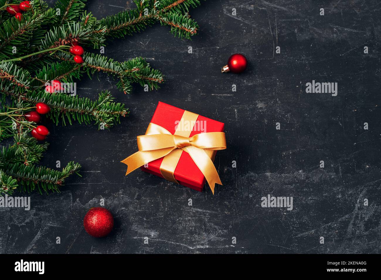 Scatola regalo rossa e rami di abete con decorazioni natalizie su tavola testurizzata nera. Concetto di vacanza invernale. Vista dall'alto, disposizione piatta. Foto Stock
