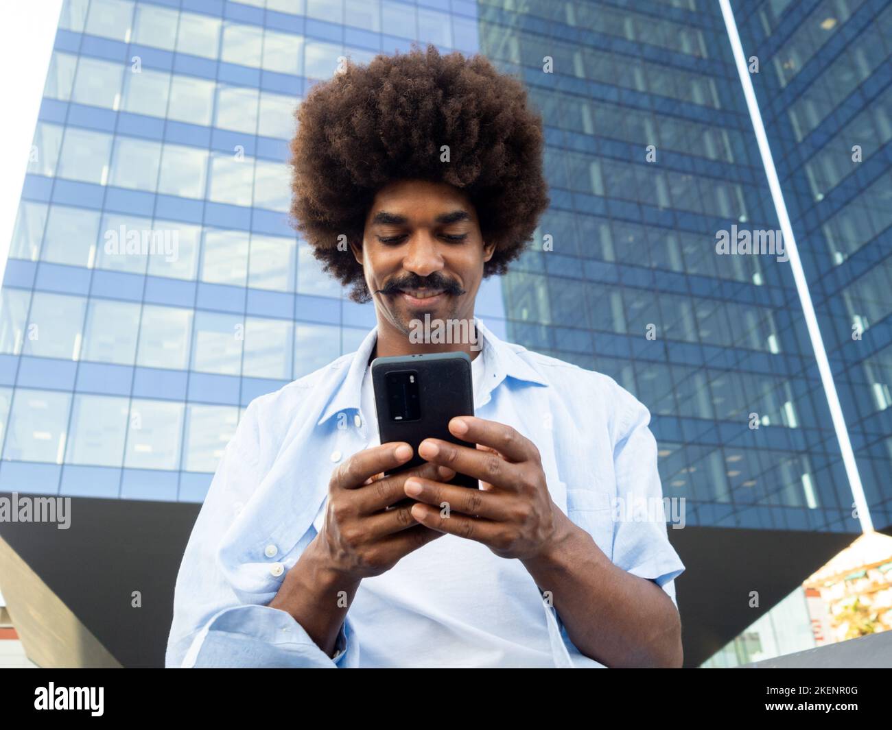 Giovane uomo afroamericano sorridente con capelli afro che chiacchiera con un telefono cellulare in una città Foto Stock