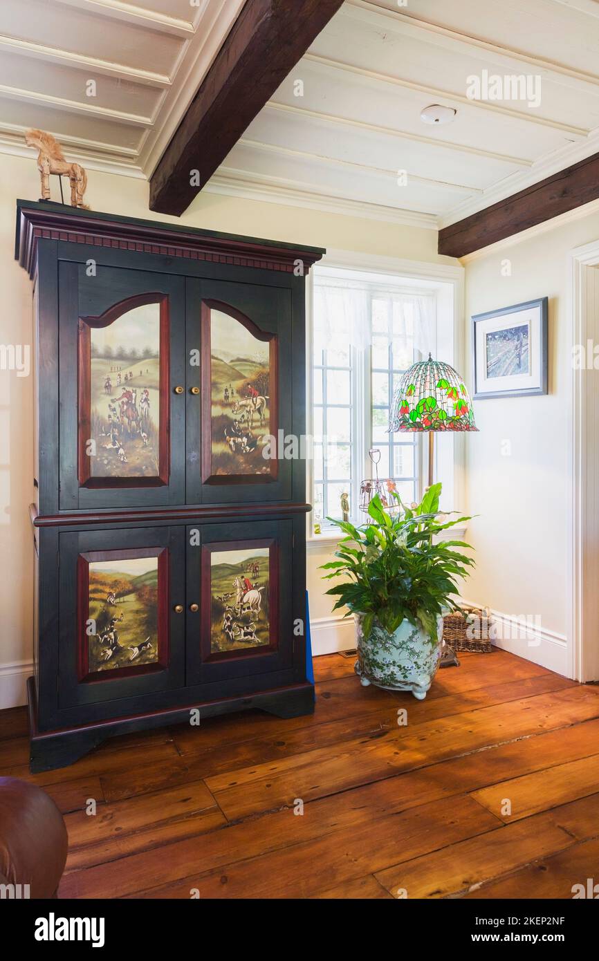 Antico armoire in legno con scene dipinte sulle porte e lampada a piedistallo tiffany nel soggiorno all'interno del vecchio stile cottage Canadiana ricostruita nel 1886 Foto Stock