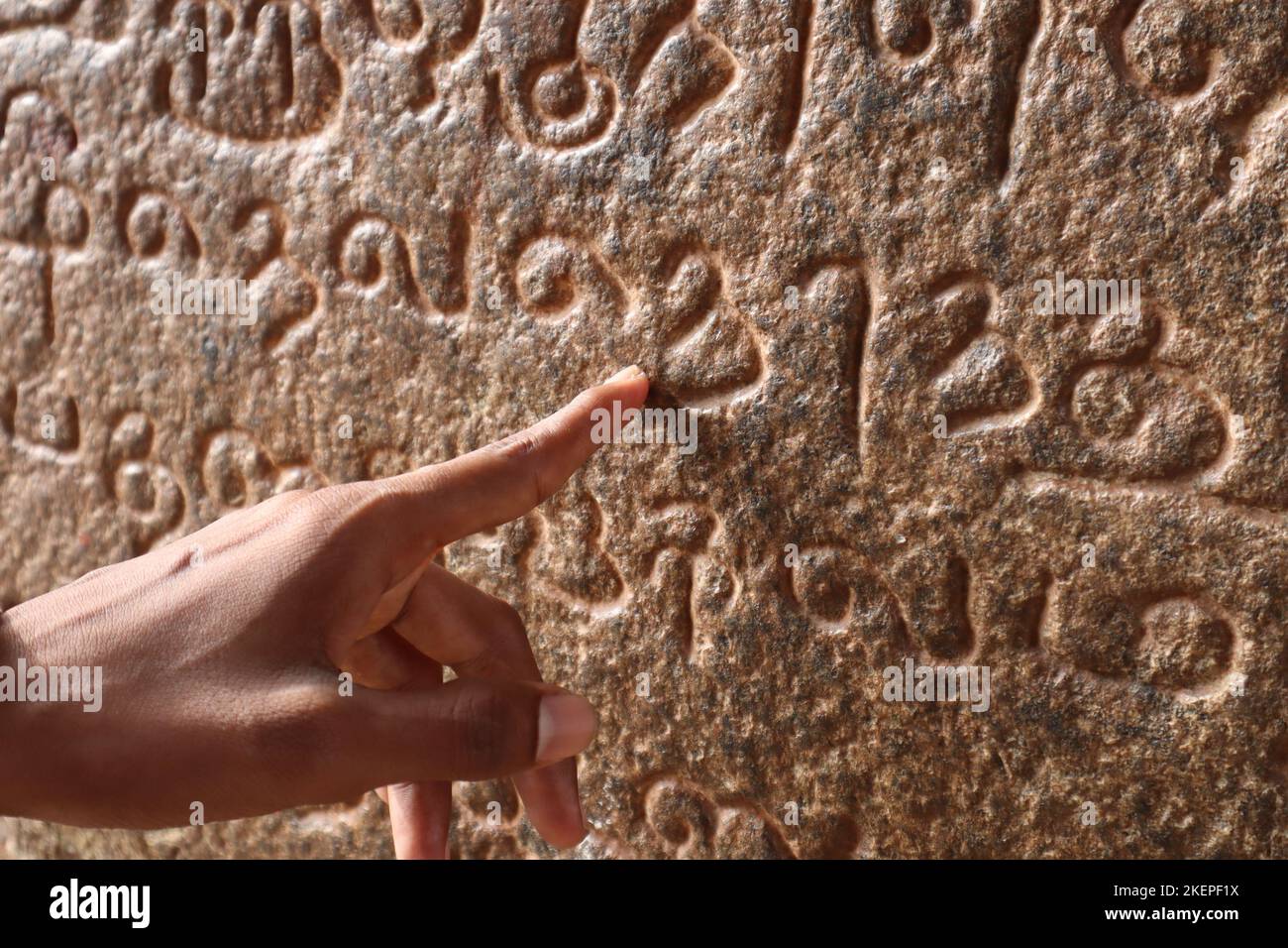 Un dito indice dell'uomo che mostra l'antico copione Tamil scolpito sulla parete del tempio Tanjore Brihadeeswarar. Foto Stock