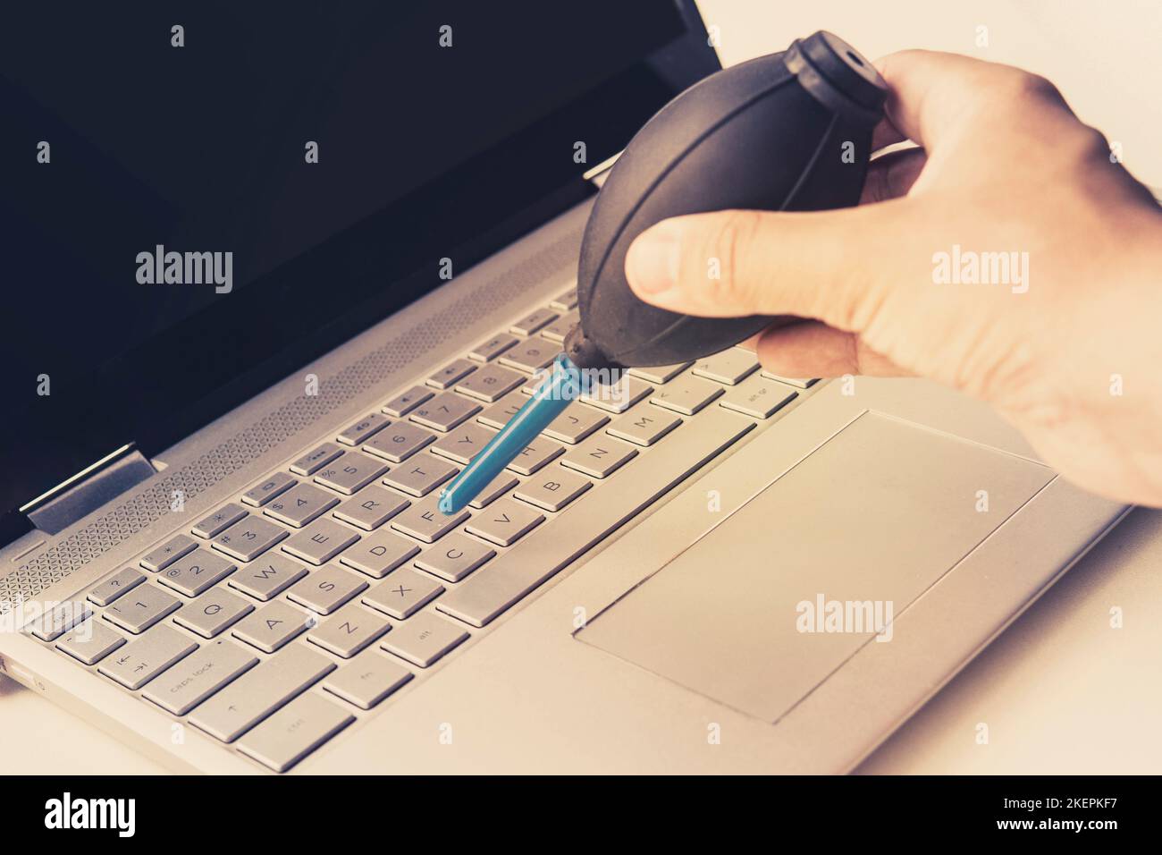 Pulizia del computer con pompa del ventilatore. Un uomo soffia i tasti della tastiera con una lampadina ad aria Foto Stock