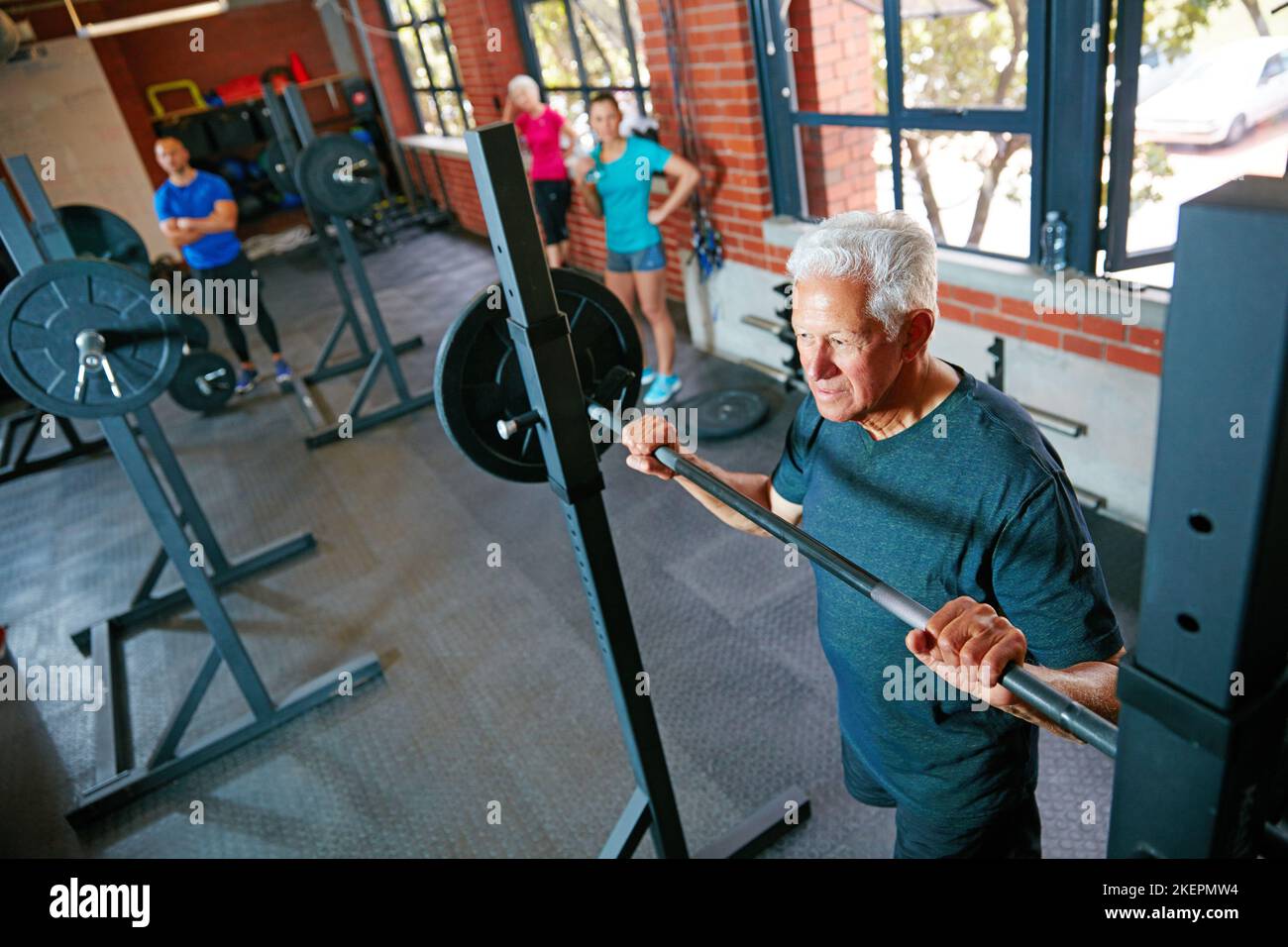 La debolezza è una scelta. Un uomo anziano che solleva i pesi mentre un gruppo della gente nel controllo di fondo sopra. Foto Stock
