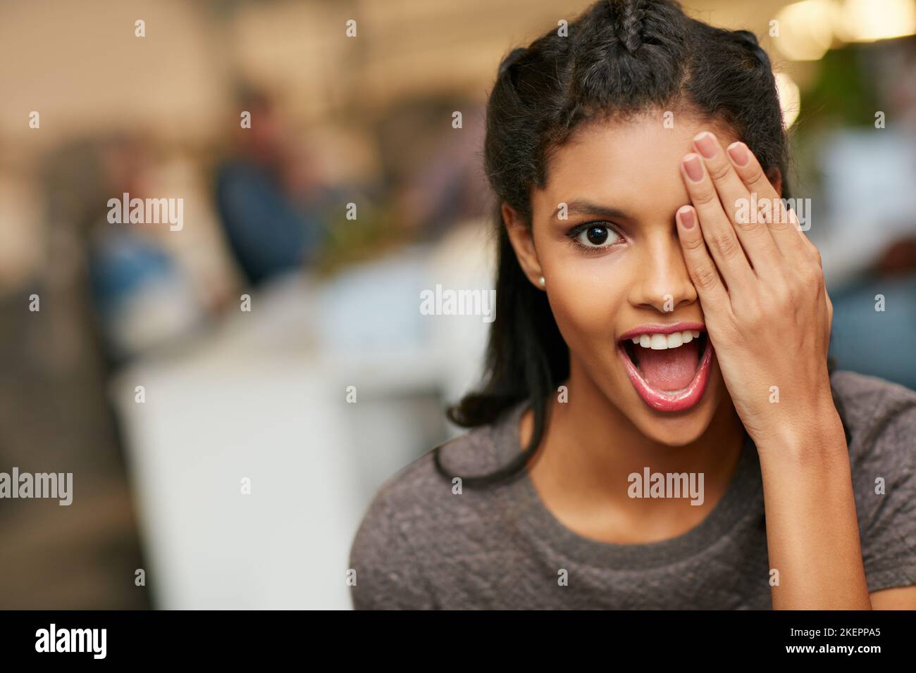 Vivacizzazione della giornata di lavoro con un momento di cuore leggero. Ritratto di una giovane donna giocosa che copre l'occhio in un ufficio moderno. Foto Stock