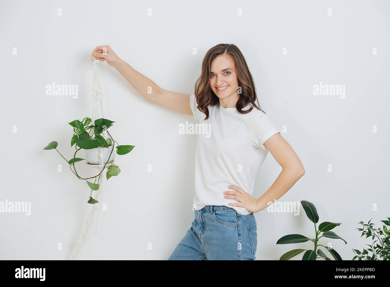 Giovane donna sorridente che tiene una pianta in vaso in macrame sospendente cestello porta. Tenendolo vicino alla parete, controllando il look. Foto Stock