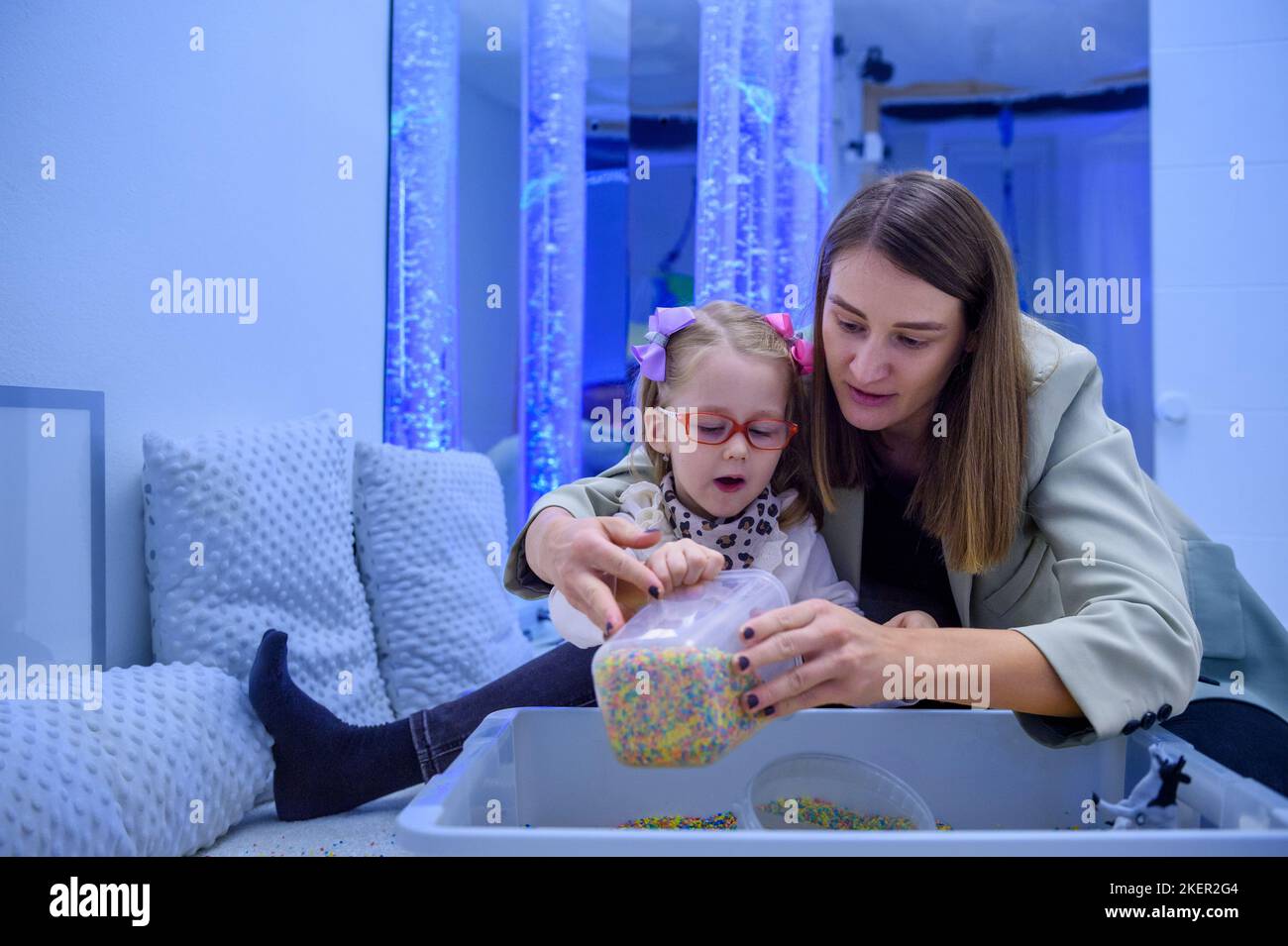 Bambino con disabilità fisica in sala stimolante sensoriale, snoezelen. Bambino che vive con la paralisi cerebrale interagendo con il suo terapeuta durante la terapia Foto Stock