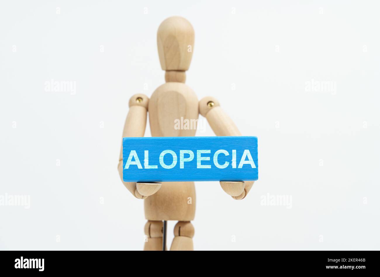 Concetto di medicina e assistenza sanitaria. Una figurina di un uomo tiene in mano un blocco di legno blu con l'iscrizione ALOPECIA. La figurina è fuori fuoco Foto Stock