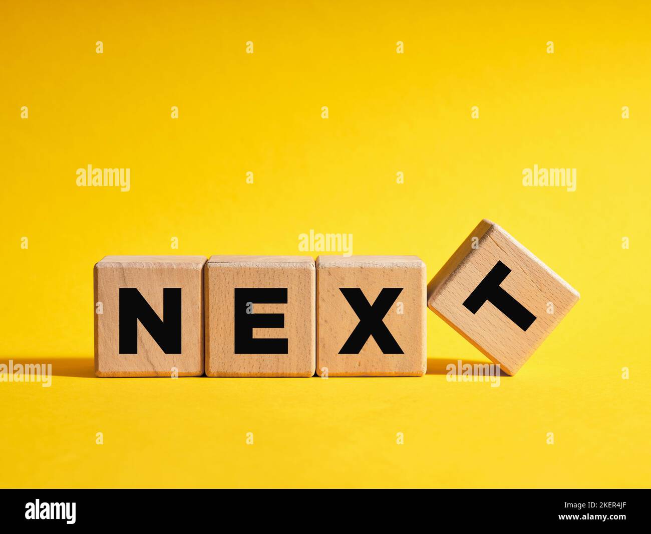 La parola Next su cubi di legno con sfondo giallo. Livello successivo o passo nel business o concetto di istruzione. Foto Stock