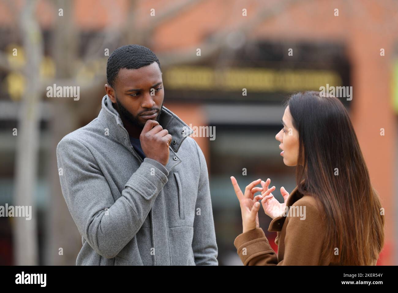 Uomo sospettoso che ascolta una donna che parla in inverno per strada Foto Stock