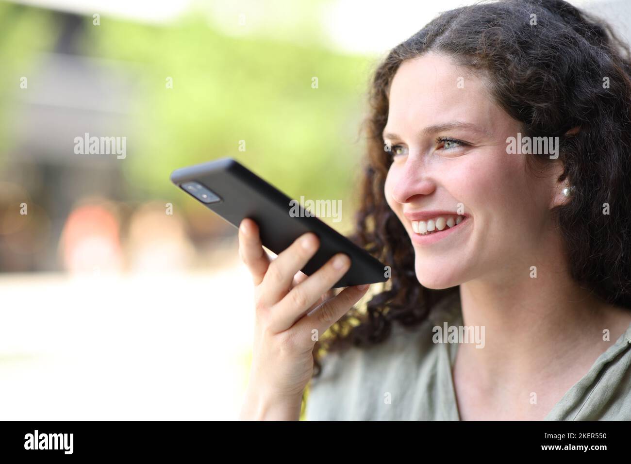 Donna felice che cammina per strada utilizzando il riconoscimento vocale sullo smartphone Foto Stock