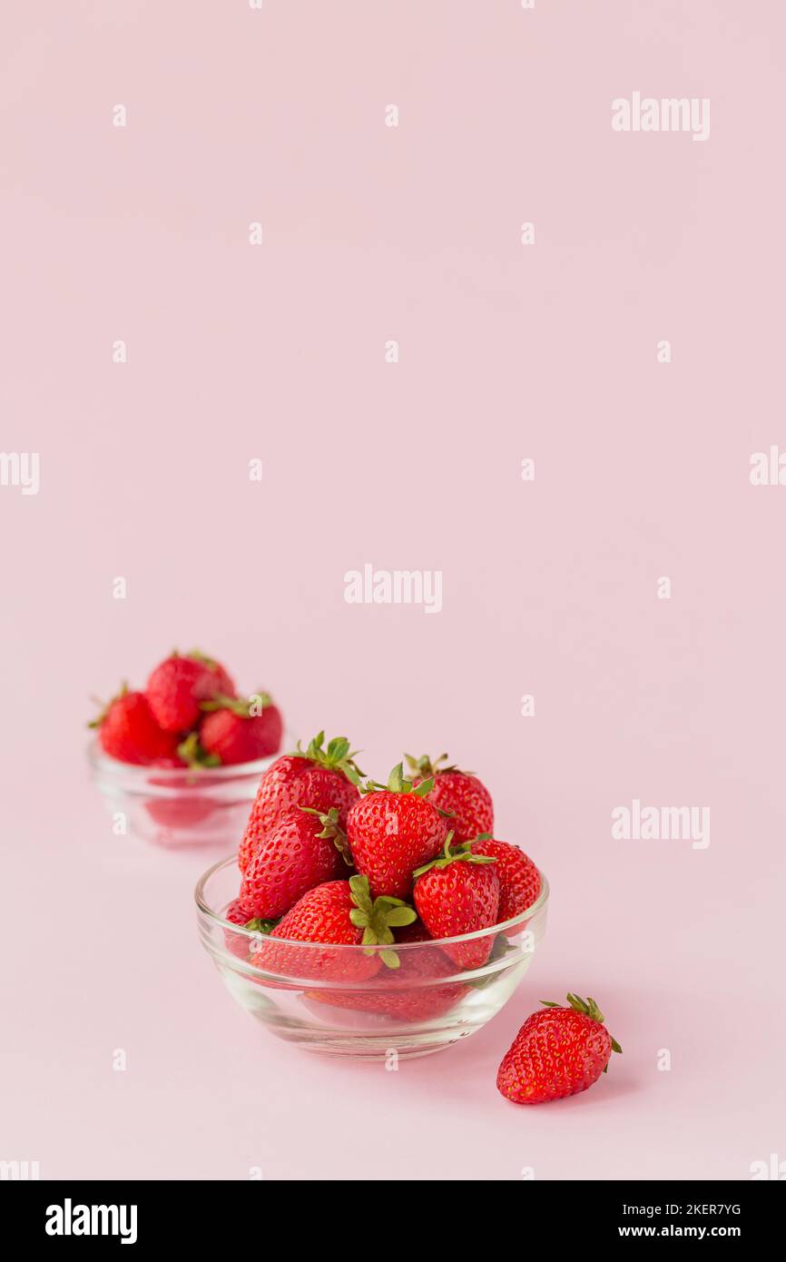 Colazione sana con frutti di bosco maturi. Fragole fresche di bellezza in recipiente di vetro su sfondo rosa chiaro. Foto Stock