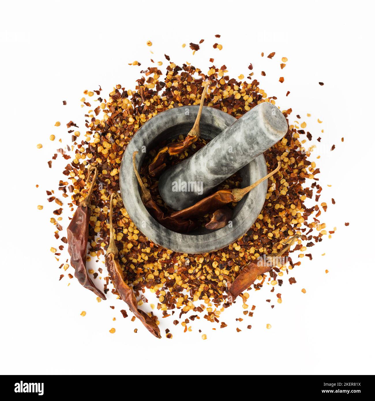 Mortaio di pietra e pestello pieno di pepe di cayenna rosso schiacciato, scaglie di peperoncino secco e semi isolati su fondo bianco. Spezie fatte in casa ingredienti Foto Stock