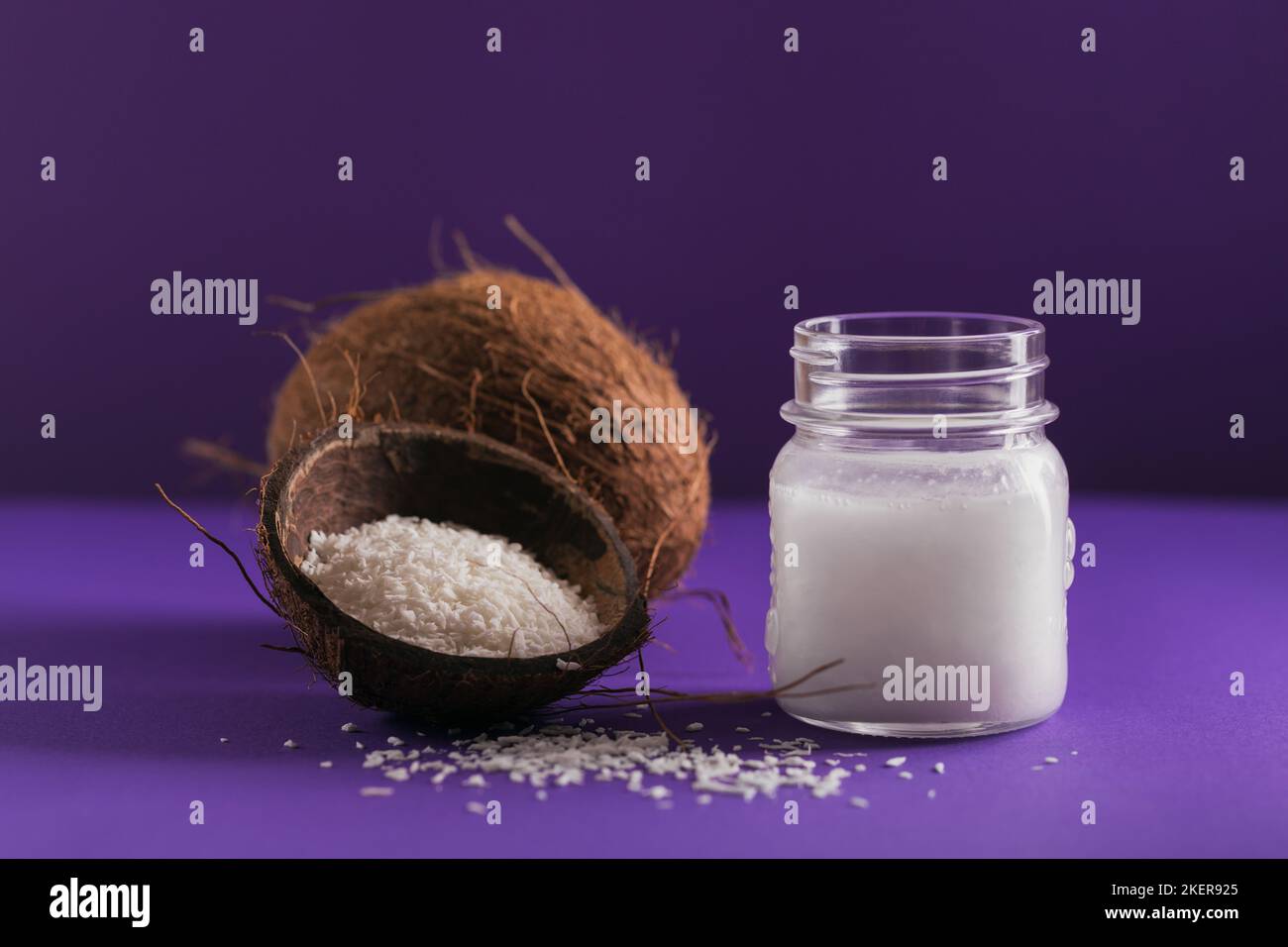 Cocco, fiocchi e olio di cocco in vaso su sfondo viola. Concetto di cucina sana Foto Stock