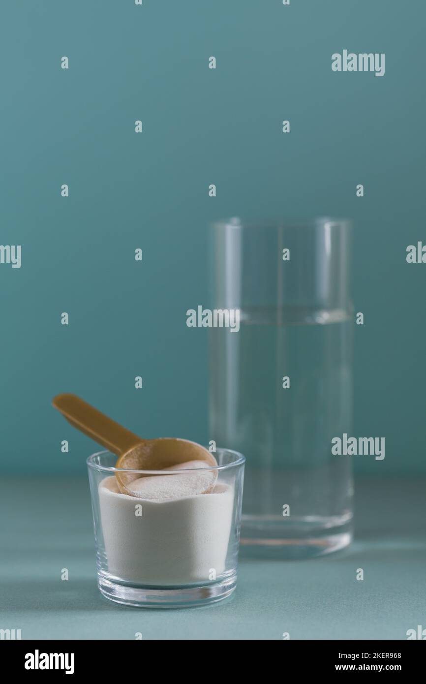 Vetro con collagene disciolto in acqua e collagene proteina in polvere su tabella di colore azzurro Foto Stock