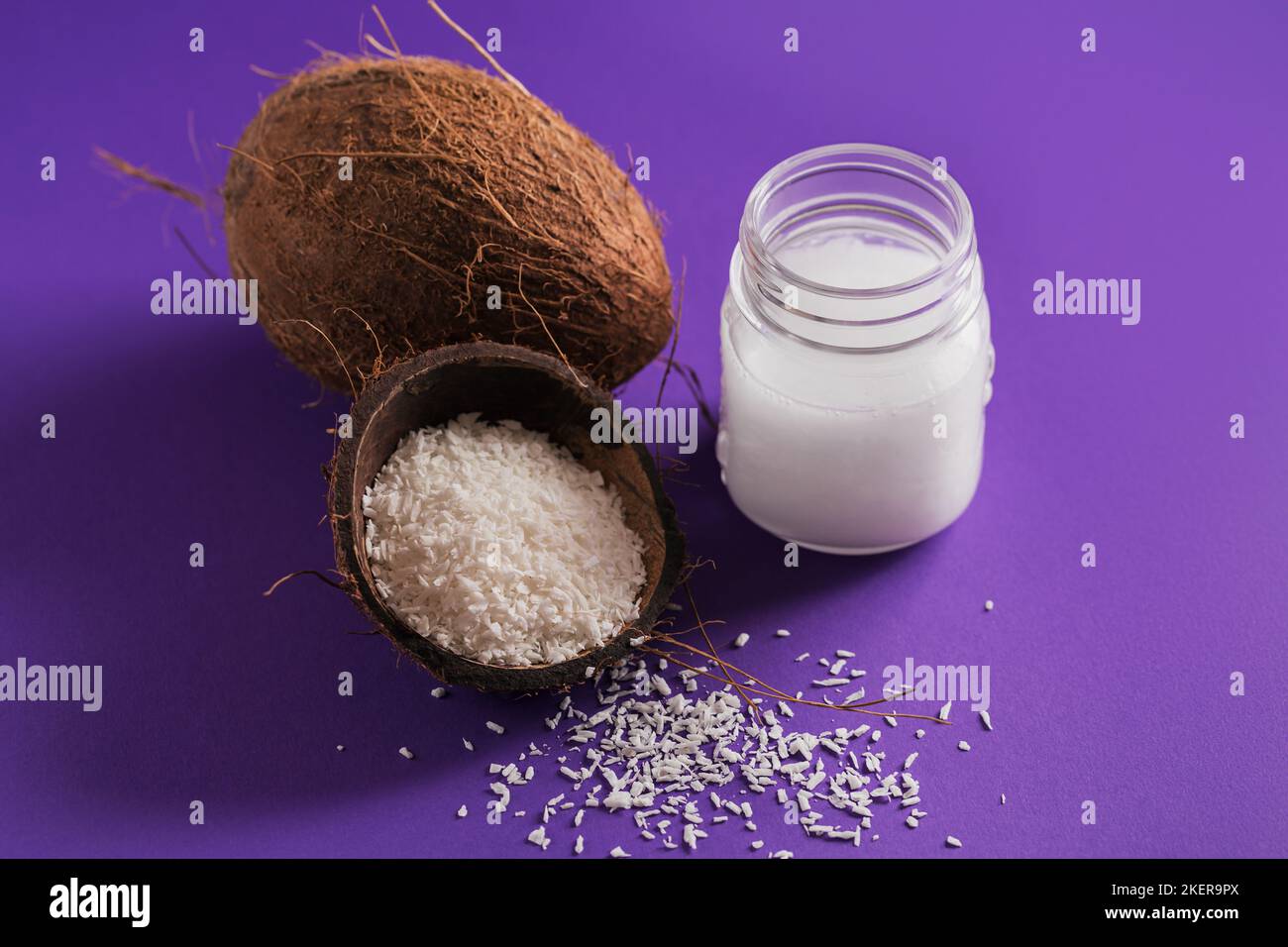 Cocco, fiocchi e olio di cocco in vaso su sfondo viola. Concetto di cucina sana Foto Stock