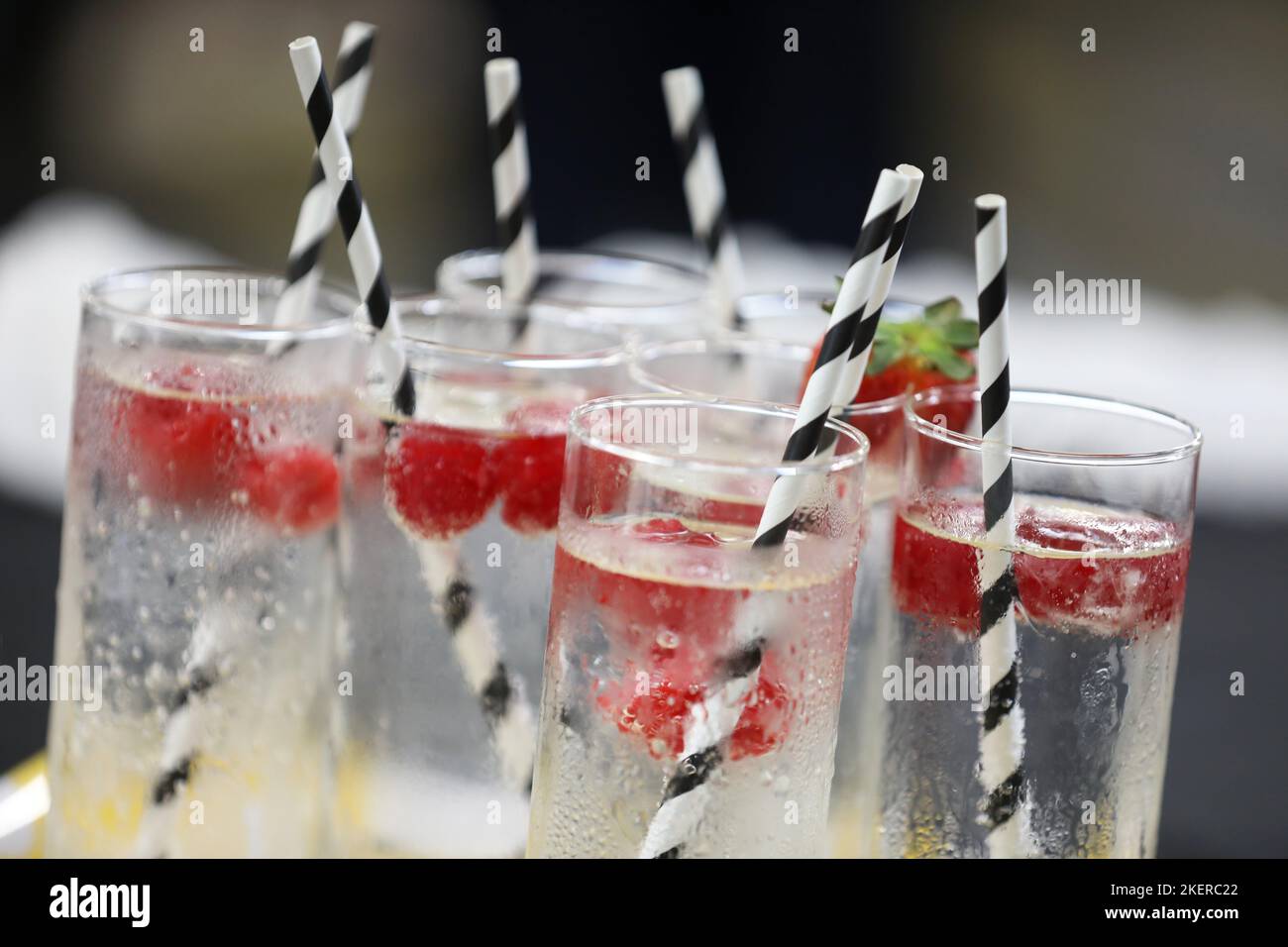 Un vassoio di alti bicchieri da bibita di vetro riempiti con acqua ghiacciata e limpida o soda guarnita con fragole e ambientazioni bianche e nere Foto Stock