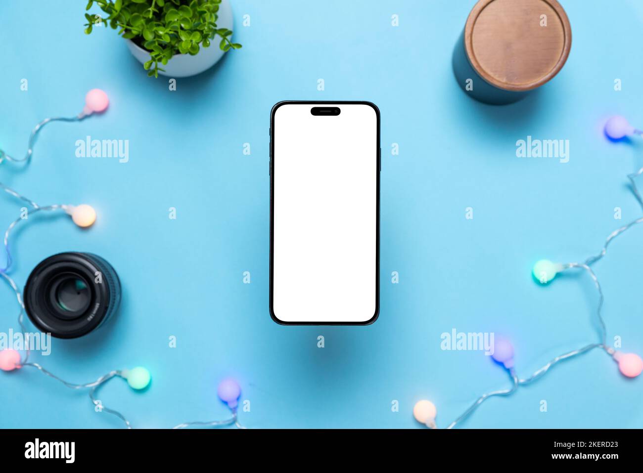 Telefono sopra la tabella blu con le lampadine colorate di festa. Display isolato per la presentazione di copia o app. Concetto di inviti di compleanno o scheda Foto Stock