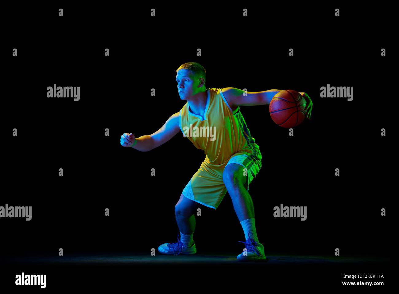Giocatore di basket professionista in azione con palla isolata su sfondo nero con filtro al neon. Dribbling. Sport, energia, abilità, squadra Foto Stock