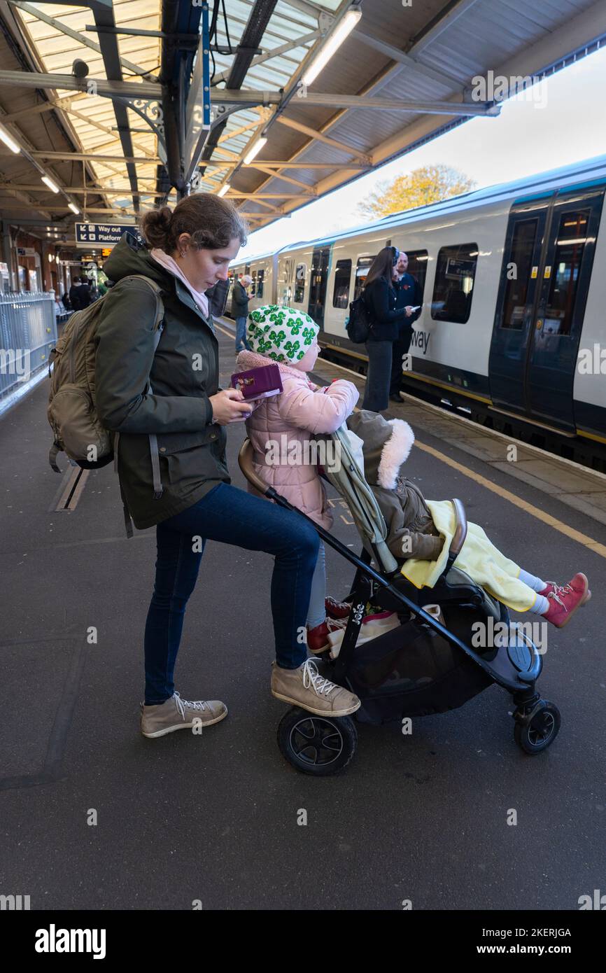 Una madre che SMS sul suo smartphone con i suoi due bambini e una sedia a rotelle, in attesa di un treno alla stazione ferroviaria di Basingstoke. Inghilterra Foto Stock