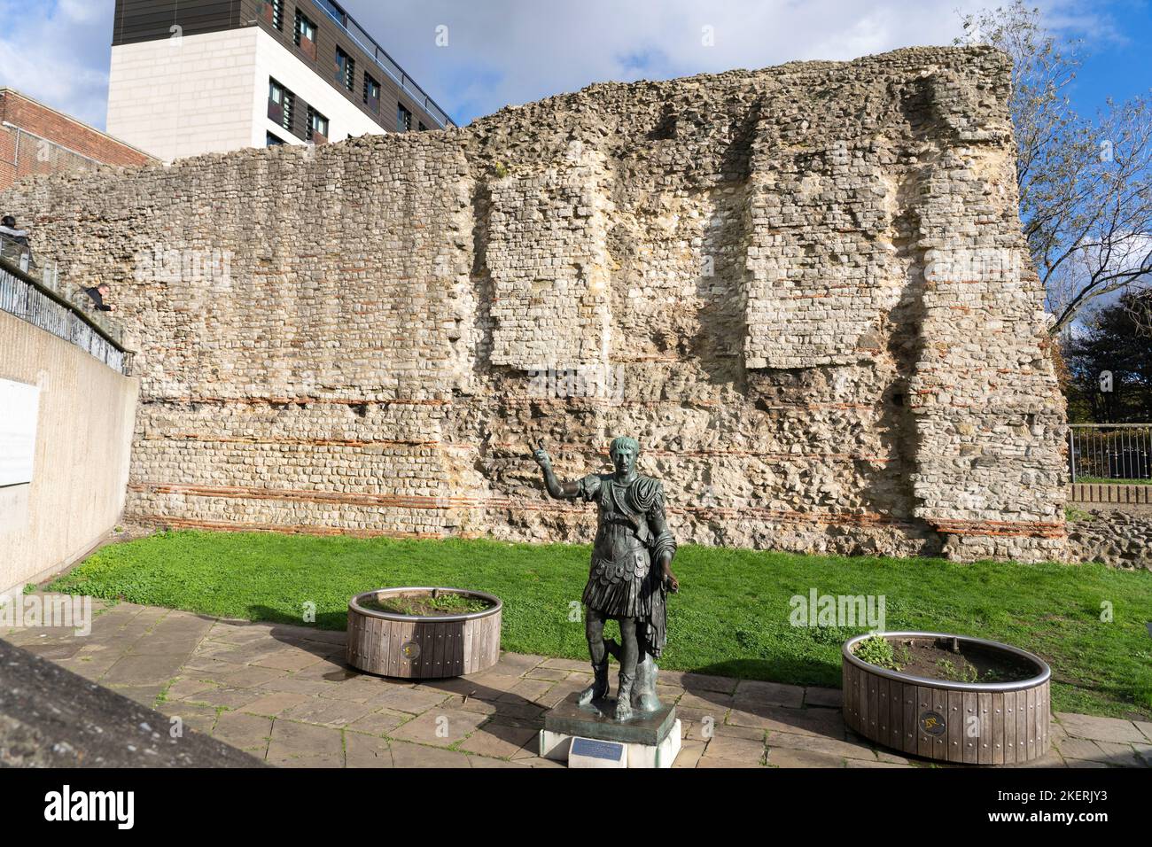 Scultura in bronzo dell'imperatore romano Traiano di fronte al Muro di Londra - antica storica cinta difensiva romana per la città portuale di Londinium Foto Stock