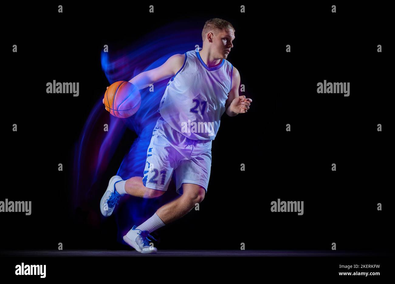 Giocatore di basket professionista in azione con palla isolata su sfondo nero con luce al neon mista. Dribbling. Sport, energia, abilità, squadra Foto Stock