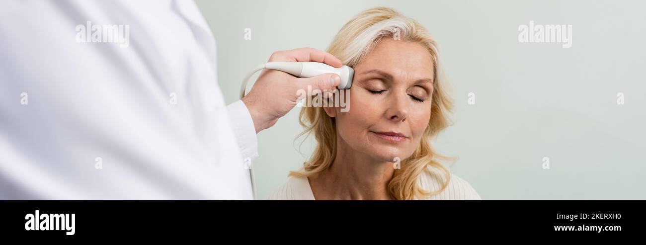 donna bionda con gli occhi chiusi vicino medico sfocato facendo ultrasuoni della sua testa, banner, immagine stock Foto Stock