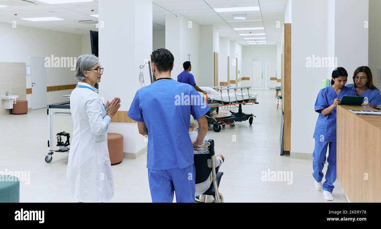 Day Hospital. Vista posteriore del corridoio clinico durante il flusso di lavoro dell'ospedale con medici, pazienti e personale medico Foto Stock