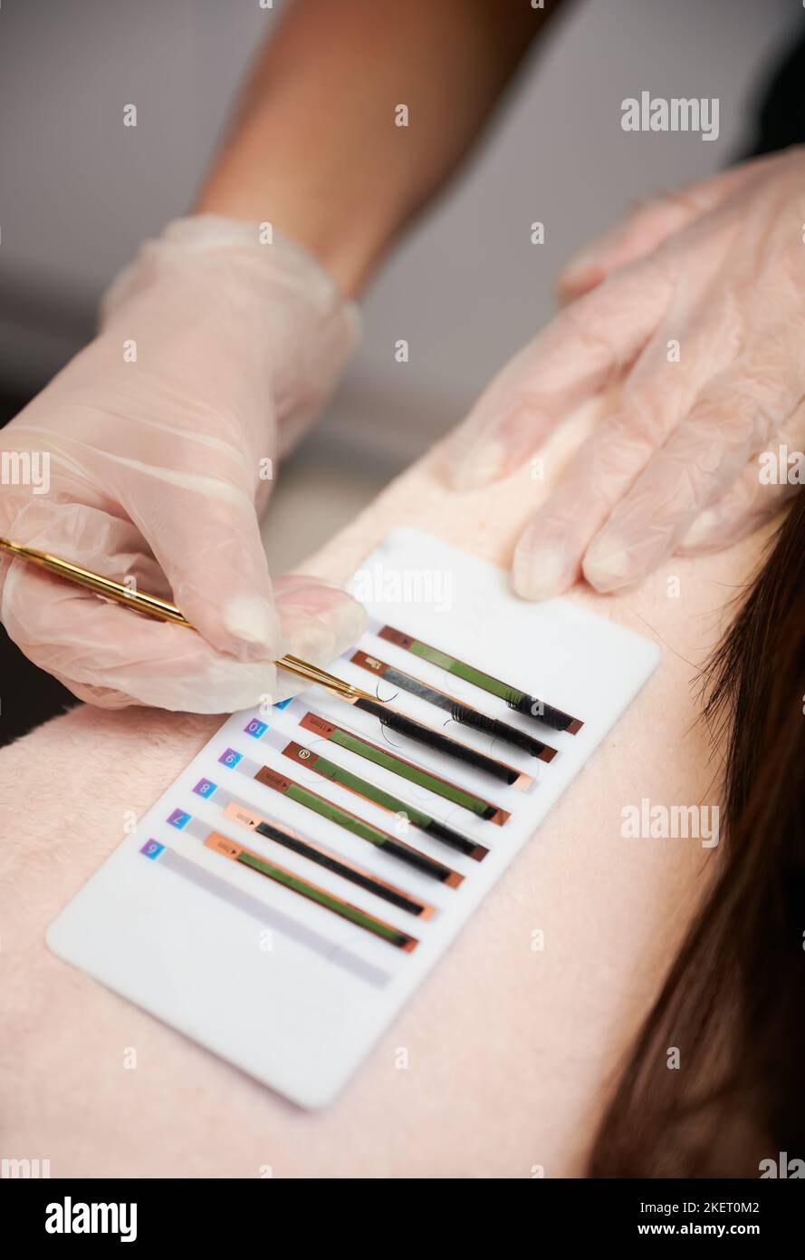Primo piano delle mani femminili in guanti sterili che raccolgono ciglia volumetriche con pinzette in acciaio inox. Tecnico di ciglia scelta ciglia per la procedura di estensione del ciglio in salone di bellezza. Foto Stock