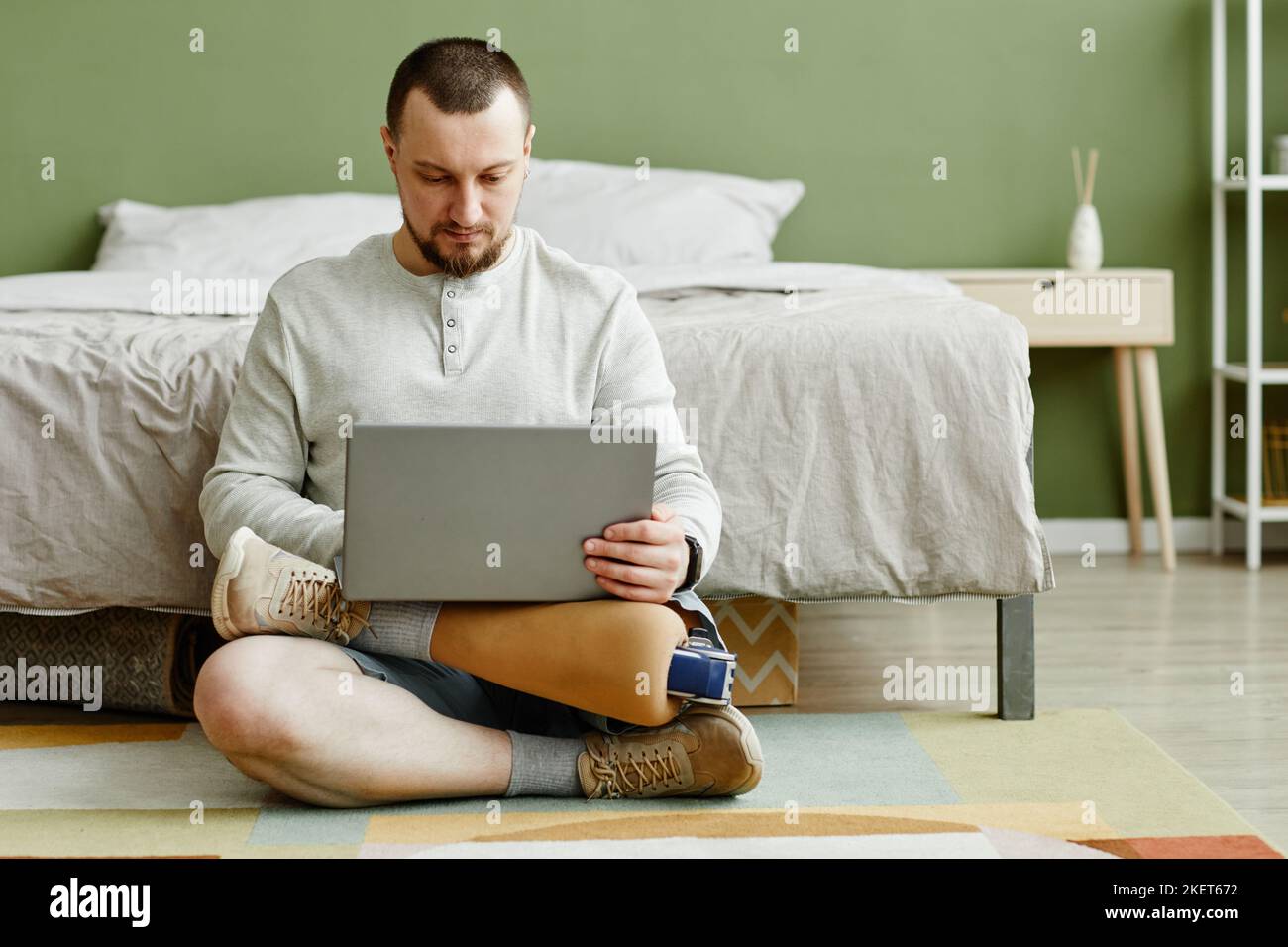 Ritratto completo dell'uomo con gamba protesica utilizzando un computer portatile mentre si è seduti sul pavimento a casa, spazio copia Foto Stock