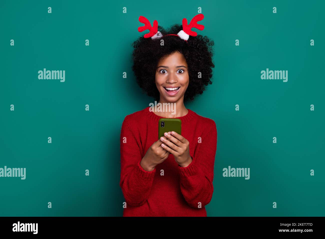 Foto di impressionato divertente piccola studentessa indossare un pullover rosso hairband chatting samsung moderno dispositivo isolato sfondo di colore verde Foto Stock