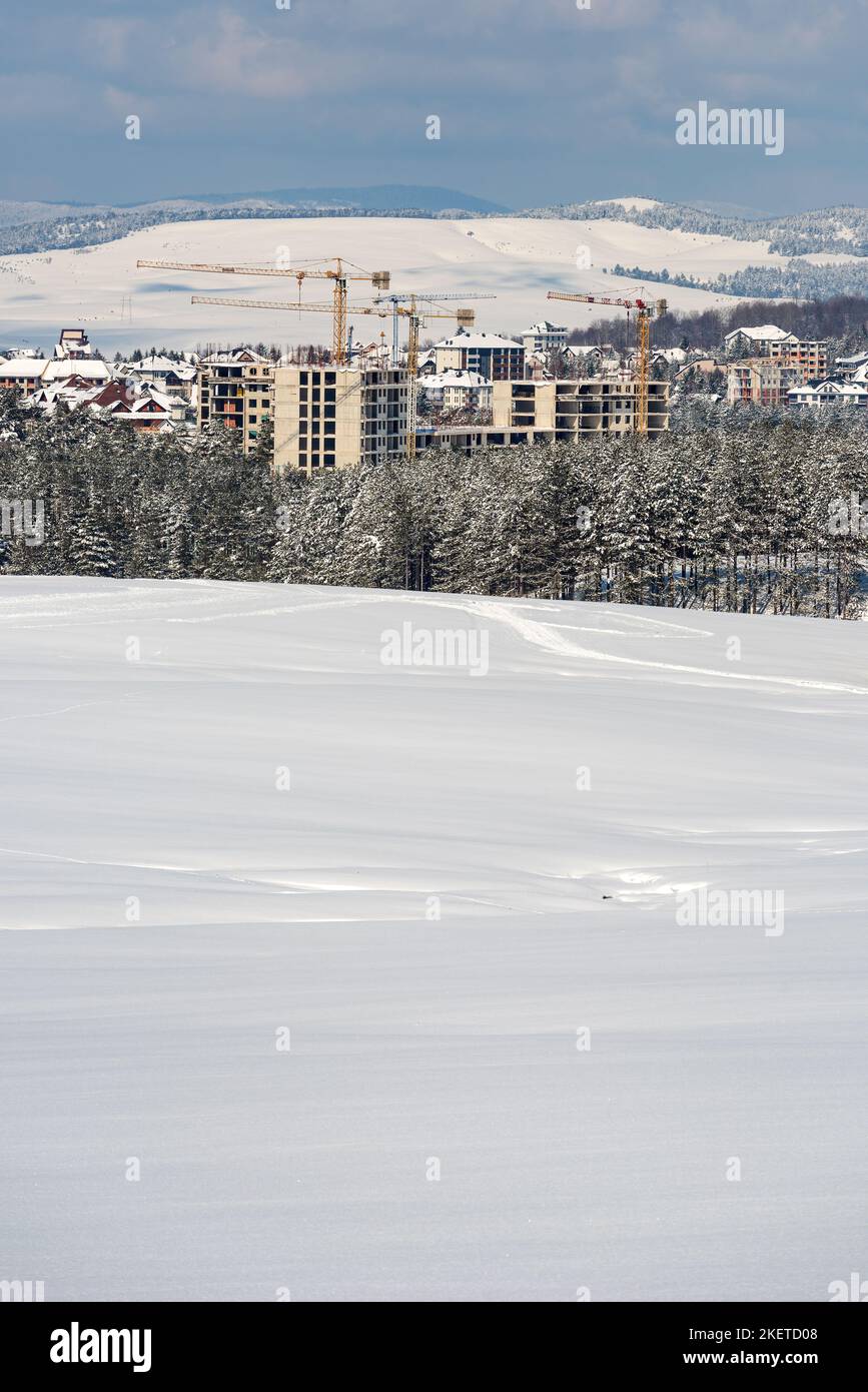 Settore edilizio sviluppo di appartamenti e alloggi a Zlatibor nella stagione invernale sotto la neve, edifici e gru che prendono il controllo della pineta Foto Stock