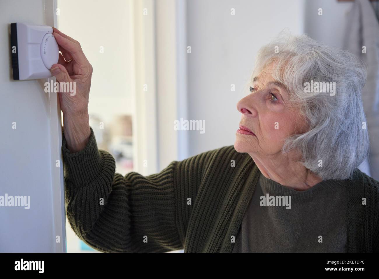 Donna anziano preoccupata che sta spegnendo il termostato centrale di riscaldamento a casa in crisi energetica Foto Stock