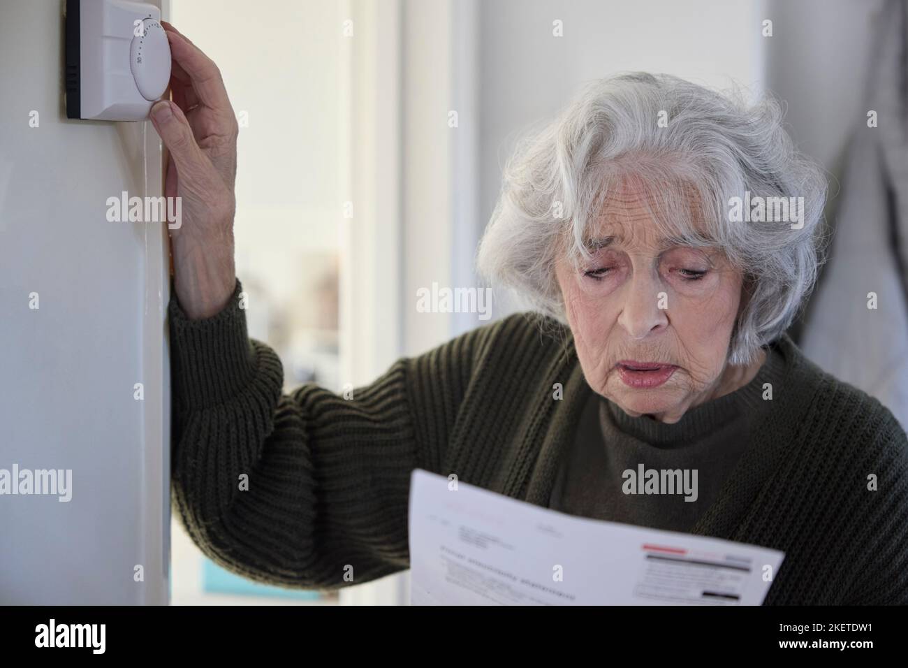 Donna anziano preoccupata con Bill che ha abbassato il termostato centrale di riscaldamento a casa in crisi energetica Foto Stock