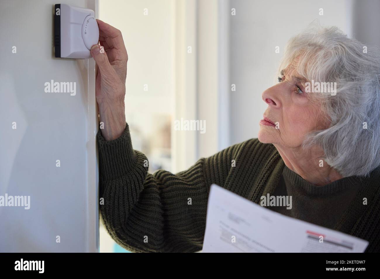 Donna anziano preoccupata con Bill che ha abbassato il termostato centrale di riscaldamento a casa in crisi energetica Foto Stock