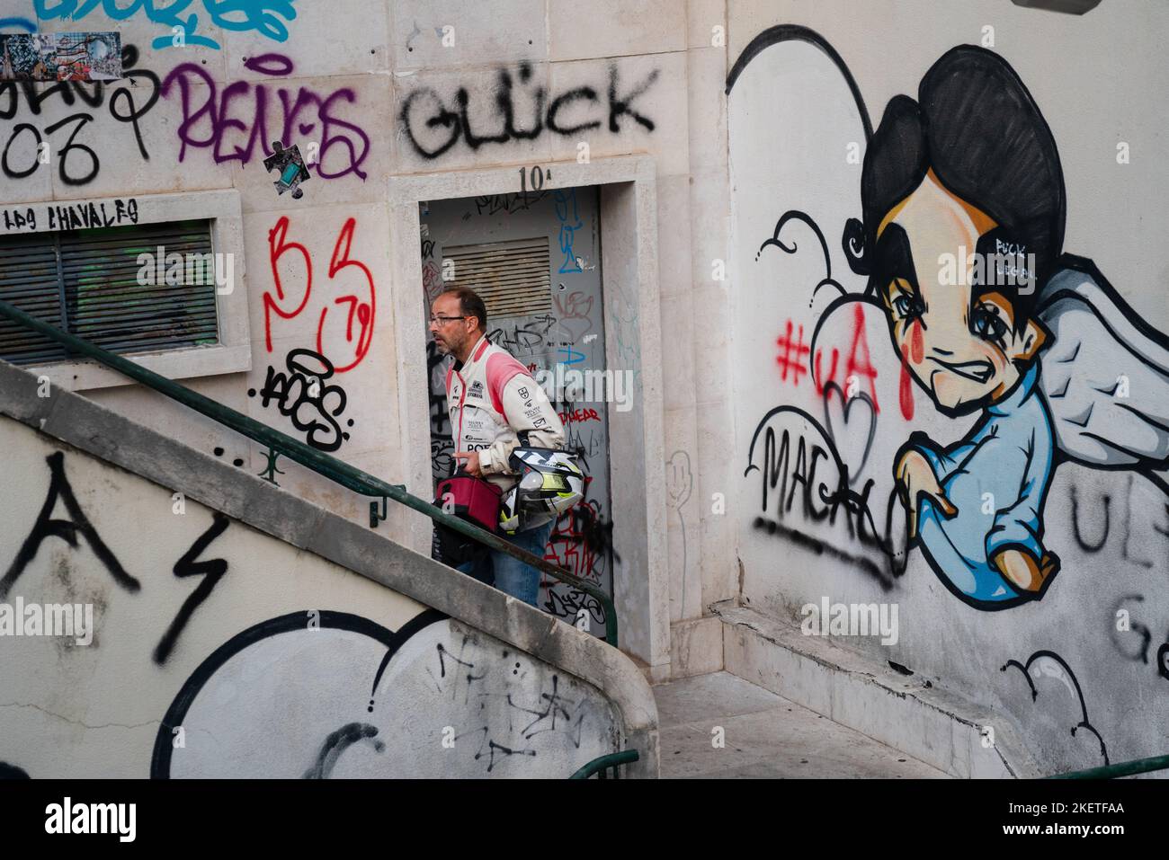 Un motociclista in moto sale gradini con pareti in cemento coperte di graffiti nel quartiere di Santa Cruz, Lisbona, Portogallo, marzo 2022. Foto Stock