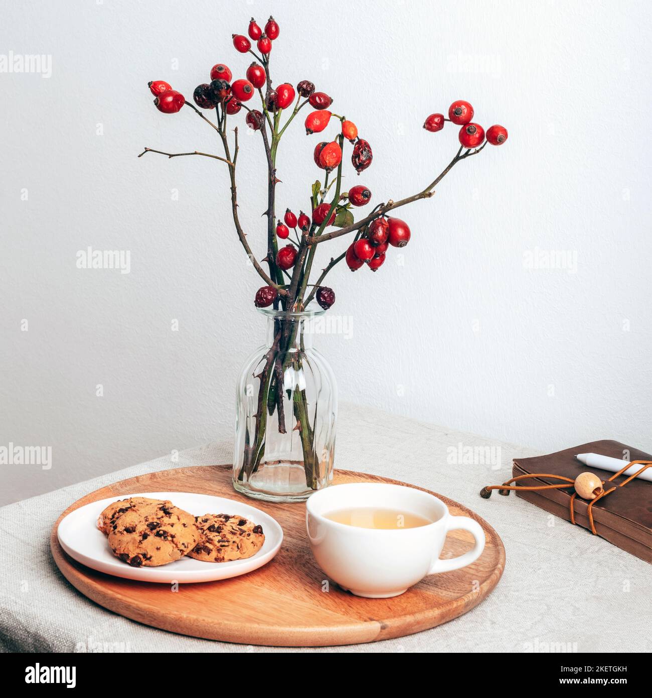 Biscotti al cioccolato e caffè su server in legno con rami di rosa in vaso di vetro. Accogliente colazione invernale. Ancora vita. Foto Stock