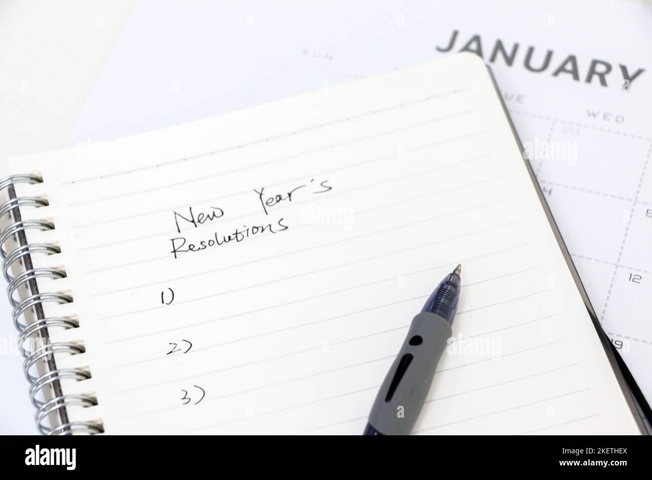 Scrivere le risoluzioni del nuovo anno, elenco su blocco note con penna a sfera, calendario di gennaio in background, focalizzazione selettiva. Fissare gli obiettivi per il nuovo anno. Foto Stock