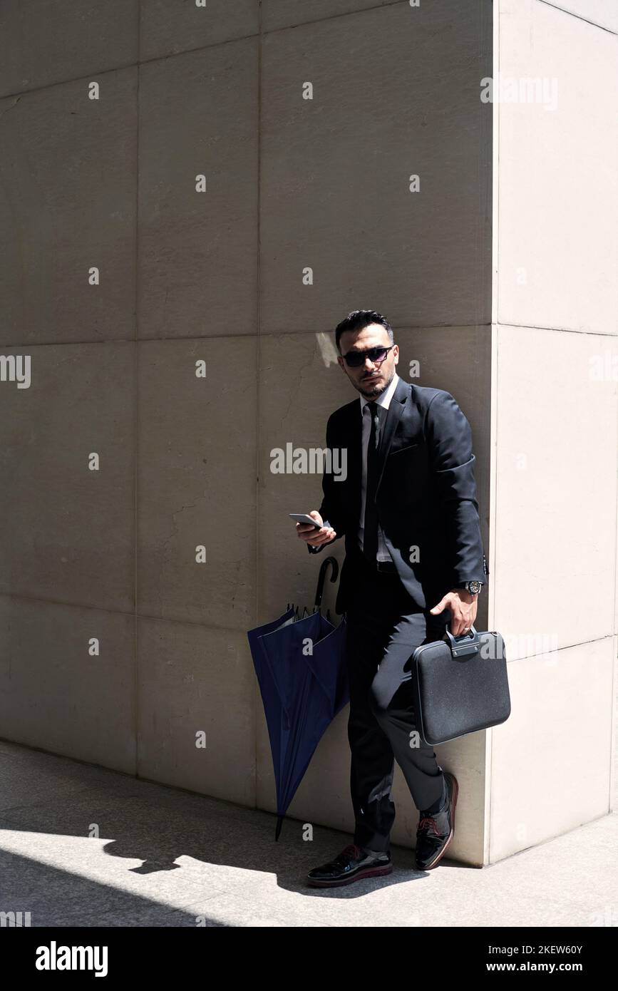 Bell'uomo elegante in occhiali da sole appoggiato alla parete dell'edificio Foto Stock