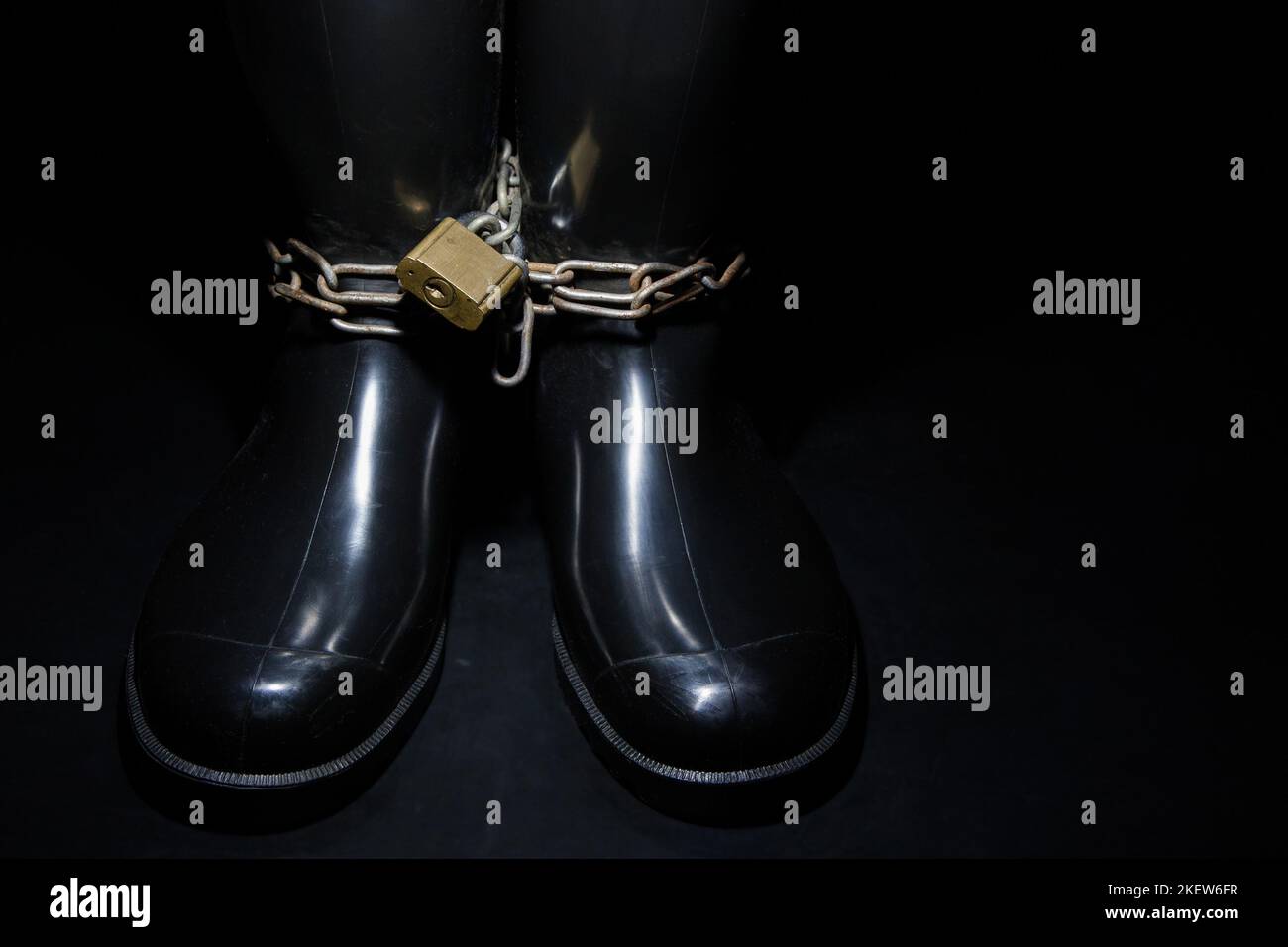 Legato con vecchie catene arrugginite in stivali di gomma nera. Foto Stock