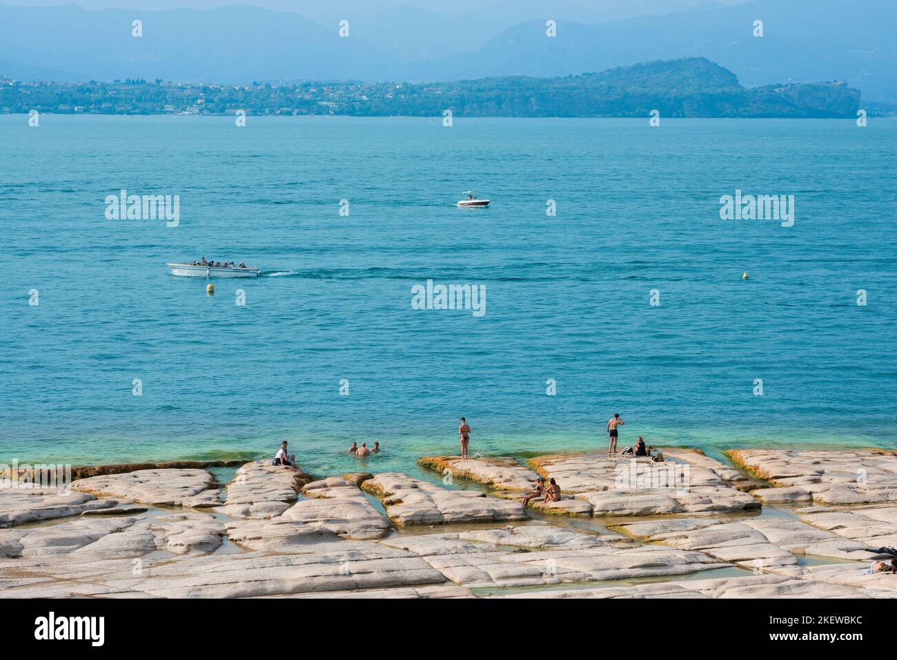 Spiaggia di Sirmione, vista in estate delle persone che prendono il sole sulla spiaggia di Giamaica sul bordo settentrionale della penisola di Sirmione, Lago di Garda, Lombardia, Italia Foto Stock