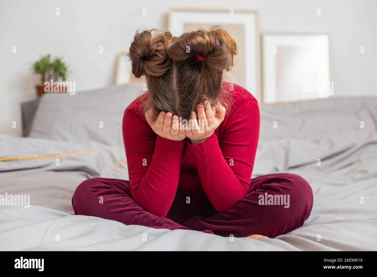 Offesa, sconvolta, piangendo ragazza caucasica si siede da sola e tiene la testa con le mani su un letto grigio. Atteggiamento negativo del bambino, ADHD Concept.Unhappy Foto Stock